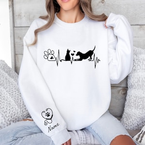 May include: White sweatshirt with a black graphic of a cat and dog with a heartbeat line and paw print. The sleeve has a stethoscope and heart with a paw print graphic and the word "Name".