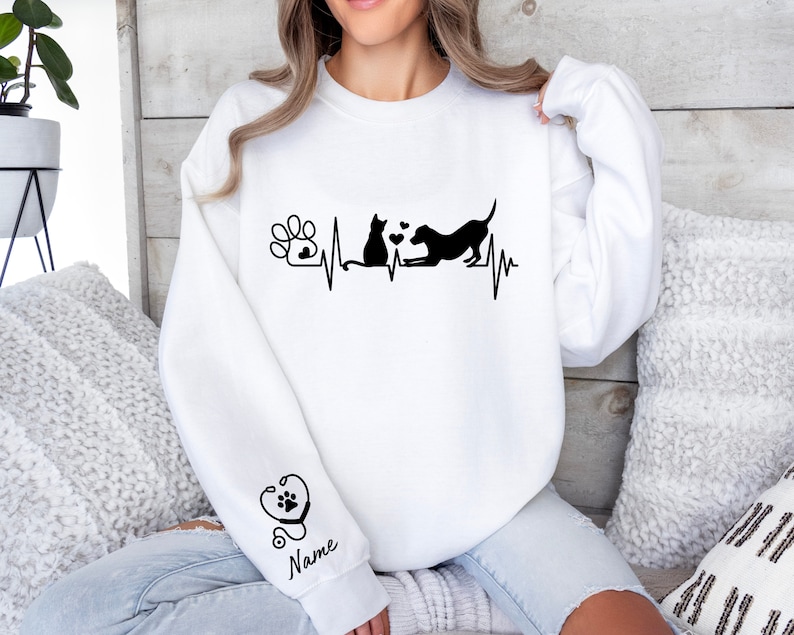 May include: White sweatshirt with a black graphic of a cat and dog with a heartbeat line and paw print. The sleeve has a stethoscope and heart with a paw print graphic and the word "Name".