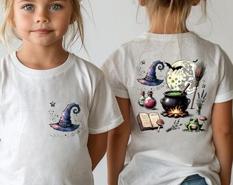 May include: Two white t-shirts with a witchy Halloween design. One shirt features a purple witch hat with a cauldron, potion bottles, and a frog. The other shirt features a smaller purple witch hat.