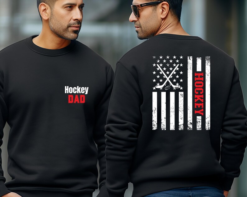 May include: Black sweatshirt with a white American flag design and the words "Hockey Dad" in red and white on the front. The back of the sweatshirt has a white American flag design with hockey sticks and a puck in the centre and the word "Hockey" in red on the right side.