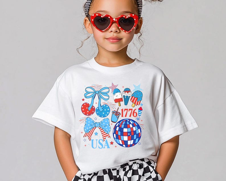 Puede incluir: Una camiseta blanca con un dise&ntilde;o patri&oacute;tico en rojo, blanco y azul. El gr&aacute;fico incluye lazos, polos de hielo, una bola de discoteca y los textos "USA" y "1776". La persona lleva gafas de sol en forma de coraz&oacute;n.