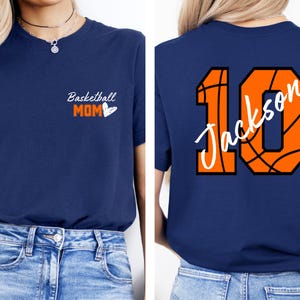 Peut inclure: Un t-shirt bleu marine avec le texte "Basketball Mom" et un c&oelig;ur sur le devant. Le dos du t-shirt a un num&eacute;ro 10 en forme de ballon de basket avec le nom "Jackson" &eacute;crit &agrave; l'int&eacute;rieur.