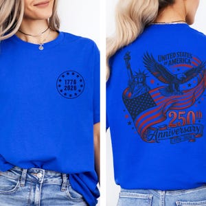 Pode incluir: Camiseta azul royal com um gr&aacute;fico circular "1776 2026" na frente. A parte de tr&aacute;s apresenta um design com uma &aacute;guia, a Est&aacute;tua da Liberdade e uma bandeira americana, com o texto "250th Anniversary".