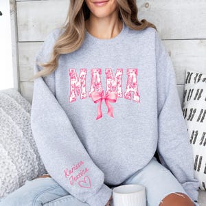 May include: Gray sweatshirt with the word "MAMA" in pink floral letters with a pink bow. The sweatshirt has the names "Karissa" and "Jessica" written on the sleeve with a pink heart.