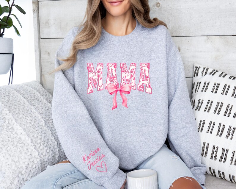 May include: Gray sweatshirt with the word "MAMA" in pink floral letters with a pink bow. The sweatshirt has the names "Karissa" and "Jessica" written on the sleeve with a pink heart.
