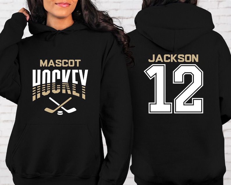 K&ouml;nnte beinhalten: Schwarzer Hoodie mit einer wei&szlig;en Grafik von gekreuzten Hockeyschl&auml;gern und dem Text "MASCOT HOCKEY". Die R&uuml;ckseite des Hoodies tr&auml;gt den Text "JACKSON 12" in Wei&szlig;.