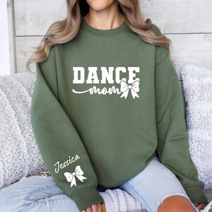 Pu&ograve; includere: Una felpa verde con la scritta "Dance Mom" e un fiocco bianco. La manica sinistra ha il nome "Jessica" e un fiocco bianco.