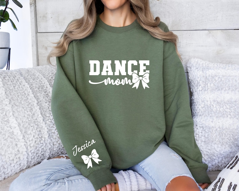 Pu&ograve; includere: Una felpa verde con la scritta "Dance Mom" e un fiocco bianco. La manica sinistra ha il nome "Jessica" e un fiocco bianco.