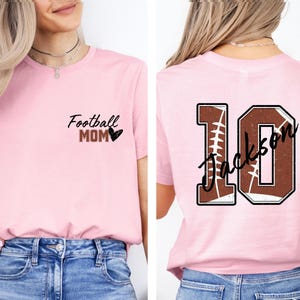 May include: Pink t-shirt with the text "Football Mom" and a heart on the front. The back of the shirt has a football-shaped number 10 with the text "Jackson" on it.