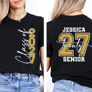 May include: Black t-shirt with "Class of 2027" in white script and gold block letters. The back of the shirt features the name "Jessica", the number "27", and the word "Senior" in white and gold.