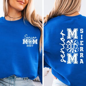 May include: Royal blue sweatshirt with white text. The front features "Senior Mom 2027" with a cheerleader graphic. The back displays "Senior Mom 2027 SIERRA" in a vertical arrangement with a cheerleader graphic.