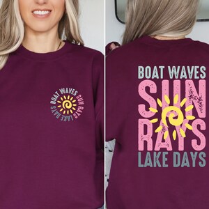 May include: Burgundy sweatshirt with a sun graphic and the text "Boat Waves Sun Rays Lake Days" in pink, yellow, and blue.