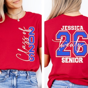 May include: Red t-shirt with white and blue text. The front of the shirt says "Class of 2026" in a script font. The back of the shirt says "Jessica 26 Twenty Senior" in a bold font.