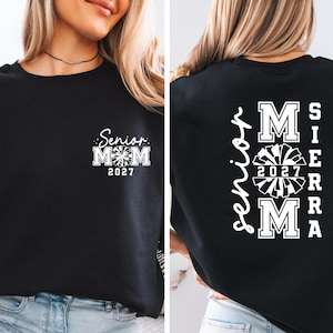 May include: Black sweatshirt with white text and a cheerleading design. The front features "Senior Mom 2027" with a pom-pom graphic. The back displays "Senior" vertically, with "MOM 2027 SIERRA MA" in a cheerleading font.