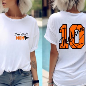 Peut inclure: T-shirt blanc avec le texte "Basketball Mom" et un c&oelig;ur sur le devant. Le dos du t-shirt a un num&eacute;ro 10 en forme de ballon de basket avec le nom "Jackson" &eacute;crit &agrave; l'int&eacute;rieur.