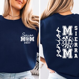 May include: Navy blue sweatshirt with white text and graphics. The front features "Senior Mom 2027" with a cheerleading graphic. The back displays "Senior Mom SIERRA 2027 MA" in a vertical layout, also with a cheerleading graphic.