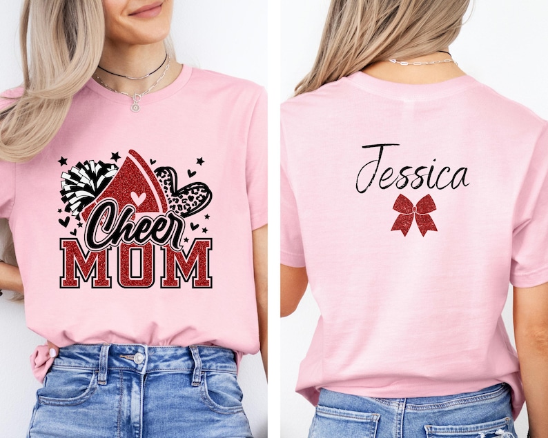 Puede incluir: Camiseta rosa de mam&aacute; de animadora con un lazo de animadora rojo con purpurina, pompones y el texto "Cheer Mom". La parte posterior de la camiseta tiene un lazo rojo con purpurina y el nombre "Jessica" en negro.