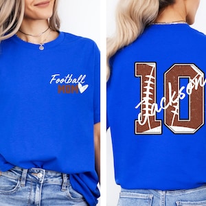 May include: Two royal blue t-shirts. One shirt has the text "Football Mom" with a heart. The other shirt has a brown football with the number "10" and the text "Jackson".