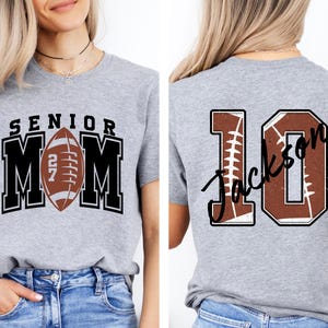 May include: A heather gray t-shirt featuring a front graphic with the text SENIOR MOM and a football replacing the letter O. The back graphic displays the number 10 with a football texture and the name Jackson written in black script across it.