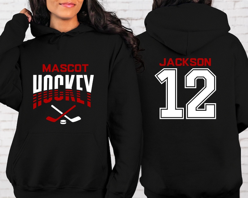 K&ouml;nnte beinhalten: Schwarzer Hoodie mit einem wei&szlig;en und roten Hockey-Design auf der Vorderseite. Der Text auf der Vorderseite lautet "Mascot Hockey". Die R&uuml;ckseite des Hoodies hat eine wei&szlig;e Nummer "12" mit roten Umrandungen und den Text "Jackson" &uuml;ber der Nummer.