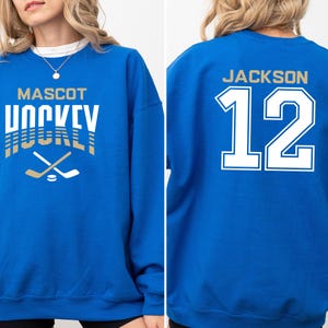 K&ouml;nnte beinhalten: Ein k&ouml;nigsblauer Pullover mit dem Text "MASCOT HOCKEY" in Gold und Wei&szlig; auf der Vorderseite und dem Text "JACKSON 12" in Wei&szlig; auf der R&uuml;ckseite.