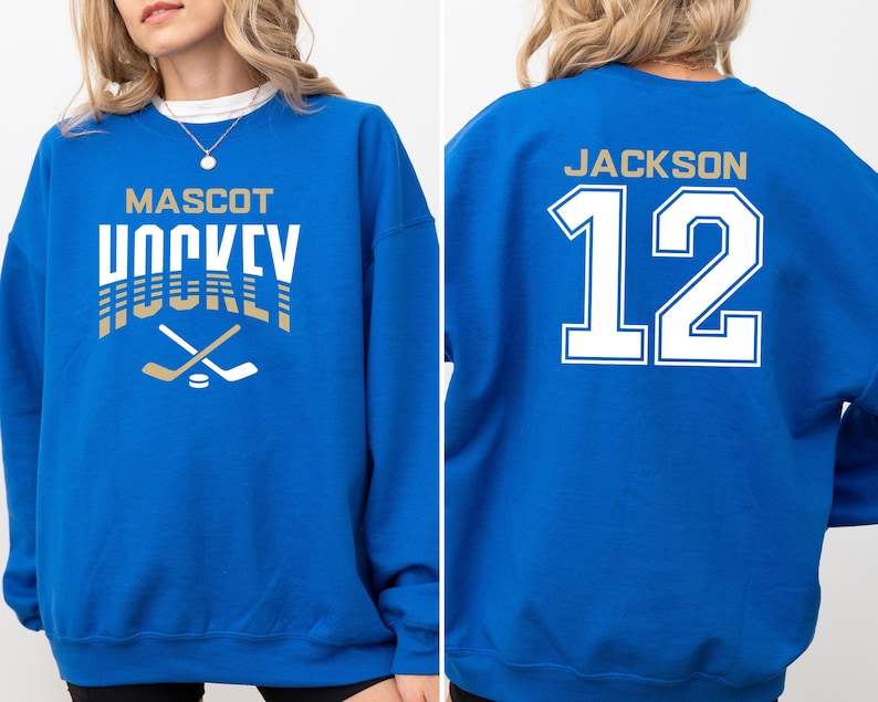 K&ouml;nnte beinhalten: Ein k&ouml;nigsblauer Pullover mit dem Text "MASCOT HOCKEY" in Gold und Wei&szlig; auf der Vorderseite und dem Text "JACKSON 12" in Wei&szlig; auf der R&uuml;ckseite.