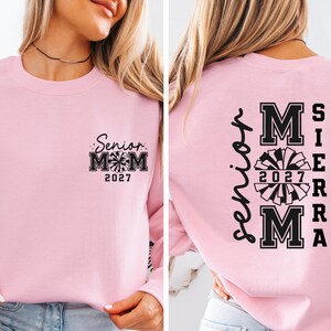 May include: A light pink sweatshirt with the text "Senior Mom 2027" and a cheerleading graphic on the front. The back of the sweatshirt has the name "Sierra" and "Mom 2027" with a cheerleading graphic.