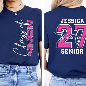May include: Navy blue t-shirt with the text "Class of 2027" in white script and pink block letters. The back of the shirt features the name "Jessica", the number "27", and the word "Senior".