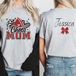 Puede incluir: Camiseta gris con un dise&ntilde;o de mam&aacute; animadora en rojo, blanco y negro en la parte delantera y un lazo rojo y el nombre Jessica en la parte posterior.