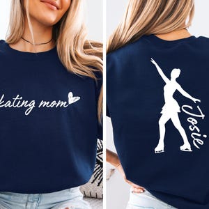May include: Navy blue sweatshirt with white text that says "skating mom" and a heart. The back of the sweatshirt has a white silhouette of a figure skater with the name "Josie" written next to it.