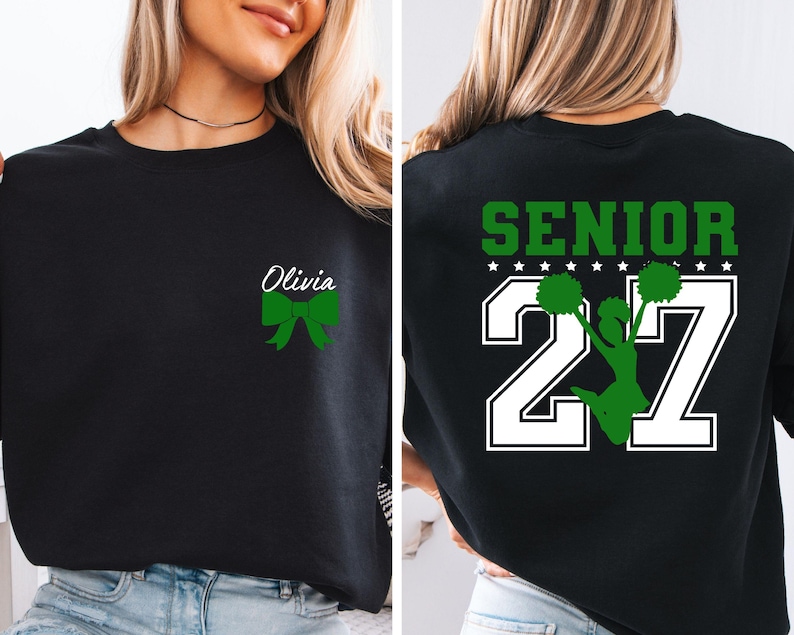 May include: A black crewneck sweatshirt featuring a small green bow and the name Olivia on the front left chest. The back displays the word SENIOR in green above the number 27 in white, with a green silhouette of a cheerleader holding pom-poms.