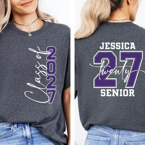 May include: Charcoal gray t-shirt with the text "Class of 2027" in white script and purple block letters. The back of the shirt features the name "Jessica", the number "27", and the word "Senior".