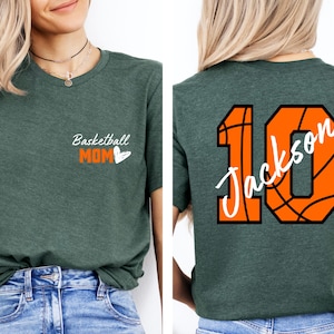 Peut inclure: Deux t-shirts verts. Un t-shirt a le texte "Basketball Mom" avec un c&oelig;ur. L'autre t-shirt a un ballon de basket avec le num&eacute;ro 10 et le nom "Jackson" &eacute;crit dessus.