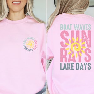 May include: Pink sweatshirt with a graphic design of a sun with the text "Boat Waves Sun Rays Lake Days" on the front and back.