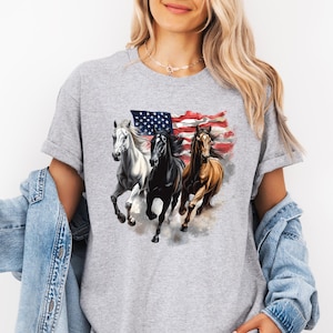 May include: A gray t-shirt featuring a graphic of three running horses in front of an American flag. The horses are white, black, and brown. The flag has red and white stripes and blue with white stars.