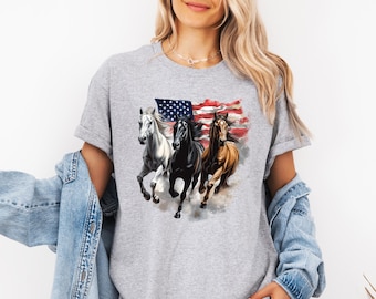 May include: A gray t-shirt featuring a graphic of three running horses in front of an American flag. The horses are white, black, and brown. The flag has red and white stripes and blue with white stars.