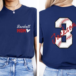 May include: Two navy blue t-shirts. The front of one shirt says "Baseball Mom" with a heart. The back of the other shirt has a white baseball number 3 with red stitching and the name "Jackson" written in red cursive.