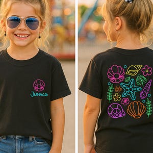 May include: Black t-shirt with a seashell design and the name "Jessica" in teal. The back of the shirt features a colorful neon design of seashells, starfish, and flowers. The shirt is worn by a young person.