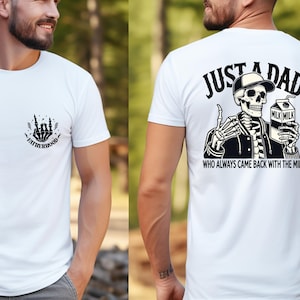 May include: White t-shirt with a black graphic on the front that says "FATHERHOOD" and a skeleton hand design. The back of the shirt features a skeleton wearing a hat and jacket, holding a milk carton, with the text "JUST A DAD WHO ALWAYS CAME BACK WITH THE MILK."