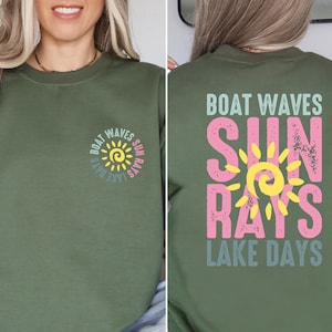 May include: A green long-sleeved sweatshirt with a sun graphic and the text "Boat Waves Sun Rays Lake Days" on the front and back.