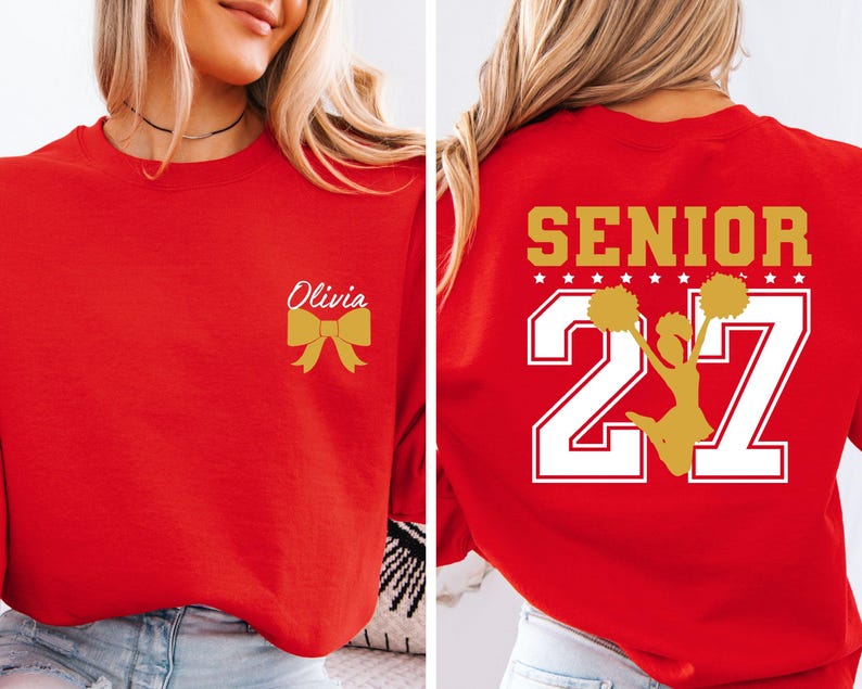 May include: A red crewneck sweatshirt featuring a gold bow and the name Olivia on the front left chest. The back displays the word SENIOR in gold, the number 27 in large white font with gold outlines, and a gold silhouette of a cheerleader.