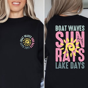 May include: Black sweatshirt with a sun graphic and the text "Boat Waves Sun Rays Lake Days" on the front and back. The sun graphic is yellow with a yellow swirl in the center. The text is in a variety of colors, including pink, blue, and green.