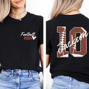 May include: Two black t-shirts with a football theme. The front shirt says "Football Mom" with a small heart. The back shirt has a large number "10" with the word "Jackson" written inside the number. The number is made to look like a football.