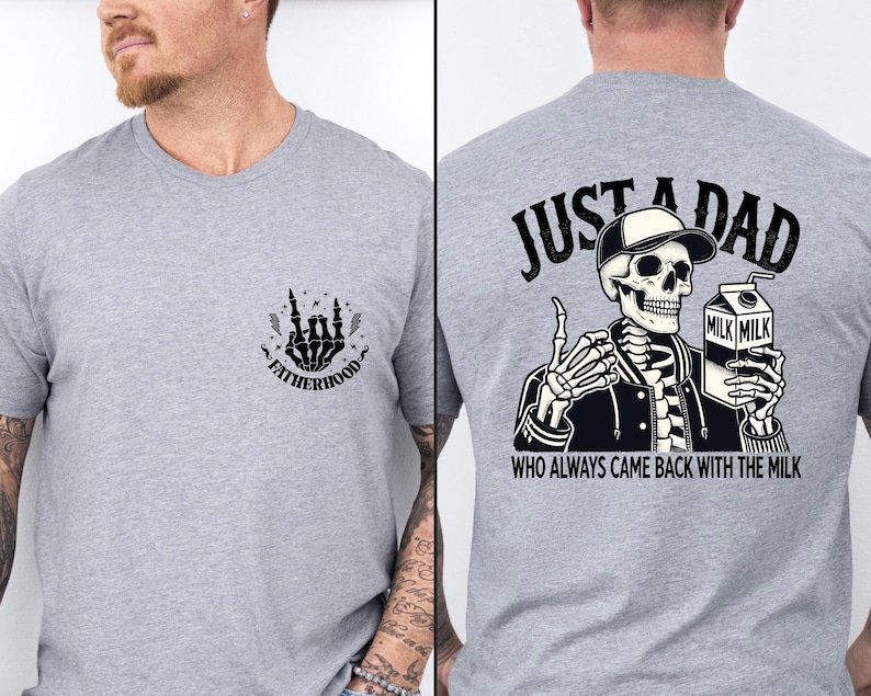May include: A light gray t-shirt featuring a skeleton graphic. The front of the shirt has a small design with the word "FATHERHOOD". The back of the shirt has a skeleton wearing a hat and holding a milk carton with the text "JUST A DAD WHO ALWAYS CAME BACK WITH THE MILK."