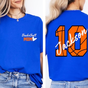 Peut inclure: Un t-shirt bleu royal avec le texte "Basketball Mom" et un c&oelig;ur sur le devant. Le dos du t-shirt pr&eacute;sente un motif de basket-ball avec le num&eacute;ro 10 et le nom "Jackson" en texte blanc.