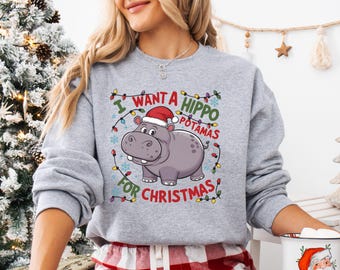 May include: A gray sweatshirt with a Christmas-themed design featuring a cartoon hippo wearing a Santa hat. The text on the sweatshirt reads "I want a hippopotamus for Christmas" with Christmas lights surrounding the text.