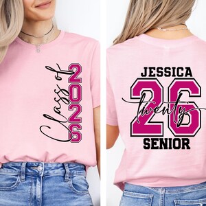 May include: Pink t-shirt with "Class of 2025" and "26" printed in black and magenta. The back of the shirt features the name "Jessica", the number "26", and the word "Senior".