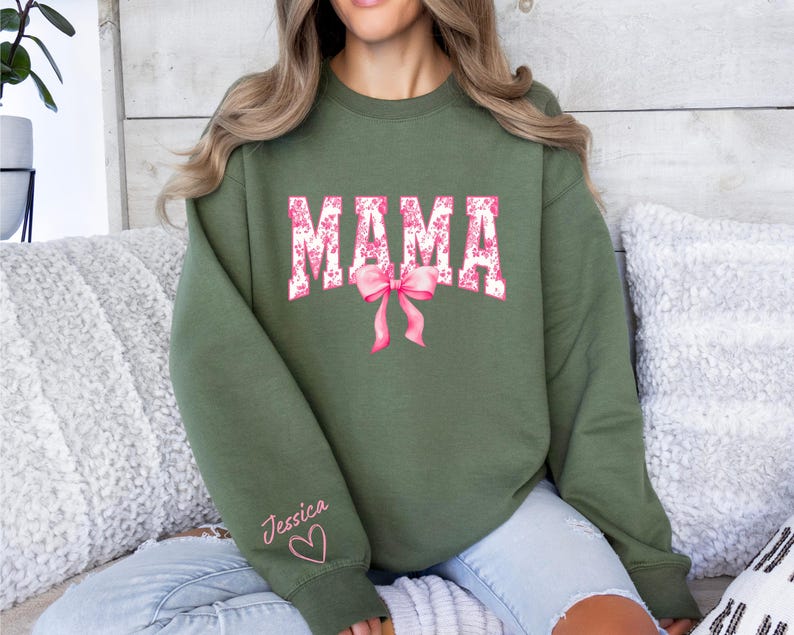 May include: A green sweatshirt with the word "MAMA" in pink and white floral print. The sweatshirt has a pink bow and the name "Jessica" written on the sleeve with a heart.