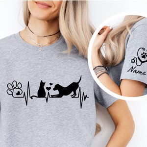 May include: Gray t-shirt with a black paw print, cat, and dog graphic with a heartbeat line. The sleeve has a black stethoscope with a paw print and the word "Name".