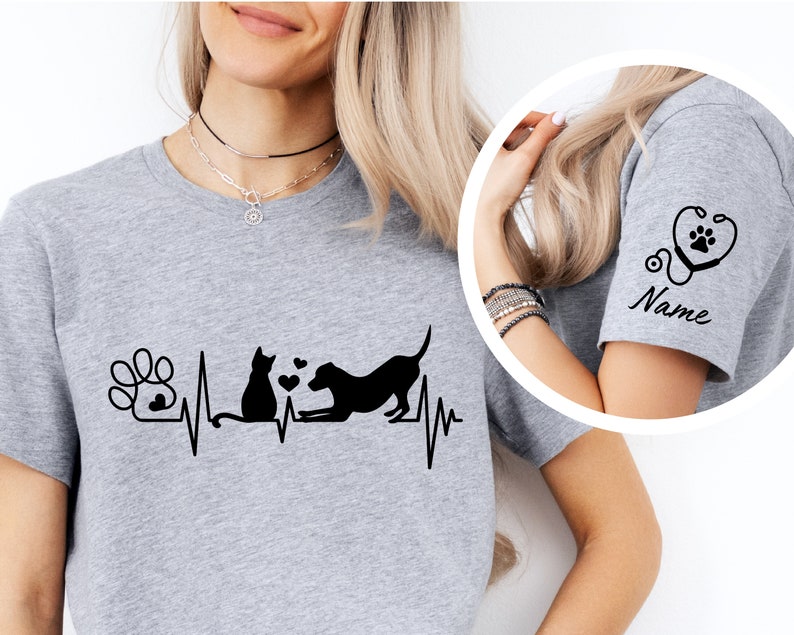 May include: Gray t-shirt with a black paw print, cat, and dog graphic with a heartbeat line. The sleeve has a black stethoscope with a paw print and the word "Name".